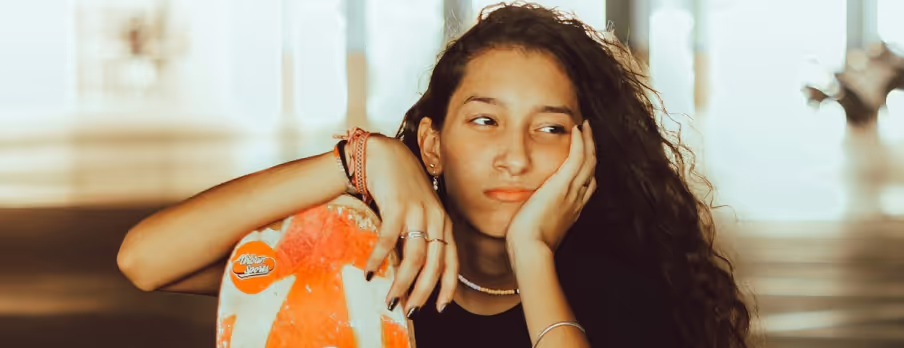 A photo used on Workshop page with a teenage girl felling bored with her hand on a skateboard
